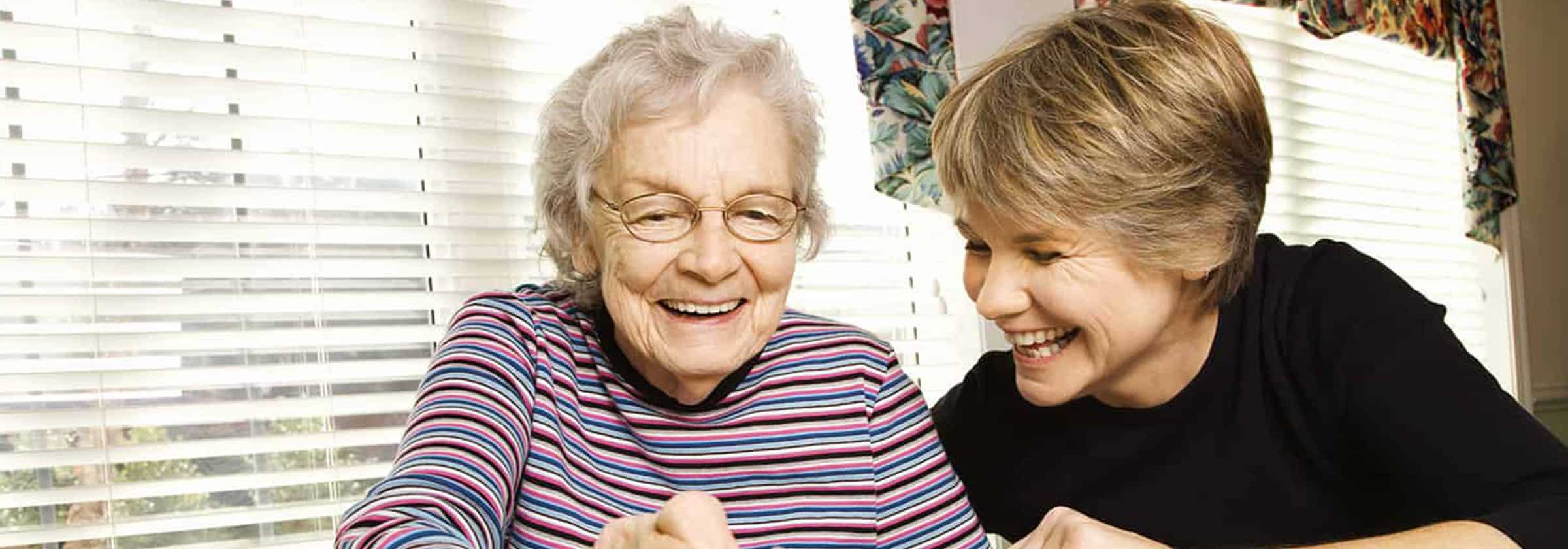 A senior memory care patient smiling and sitting with a nursing assistant