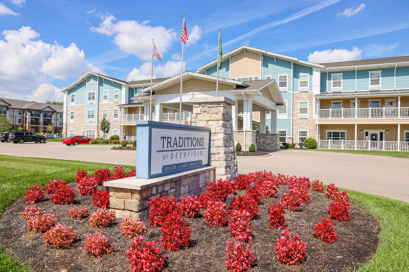 View of Traditions of Deerfield from the front entrance by the main sign with a flowerbed full of red flowers